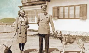 Eva Braun, hitlers fru, står med en hund. Bredvid henne står en man i uniform med en annan hund.