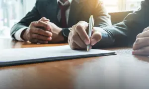 Menedżer podpisuje kontrakt. Dłoń z długopisem nad dokumentem, druga dłoń złożona na stole.