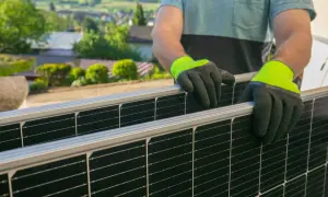 Un técnico de placas solares instala paneles en un tejado con vistas a un pueblo.