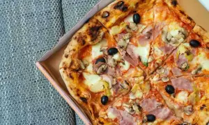 Pyszna pizza capricciosa z szynką, pieczarkami, oliwkami i karczochami, prosto z pieca, w pudełku.