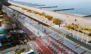 Nowoczesna promenada nad morzem, z piaskiem, wydmami i łagodnymi falami. Ludzie spacerują, ciesząc się chłodnym dniem.
