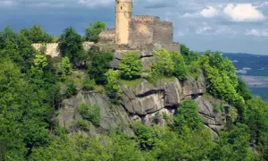 Zamek Chojnik góruje nad skalistym zboczem, otoczony bujną zielenią drzew.