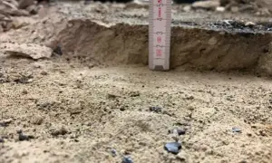 Mesure de la profondeur du décaissement du sol avec une règle. Le sable et les débris sont visibles.
