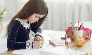 Niña concentrada en su dictado 2 primaria, rodeada de útiles escolares, un libro abierto y una manzana.