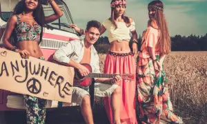 Neo-Hippies mit Gitarre und Schild "Anywhere" vor einem Van in einem Feld.