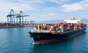 Großer Frachter mit bunten Containern verlässt den Hafen. Kräne im Hintergrund, die auf die nächste Lieferung duty unpaid warten.
