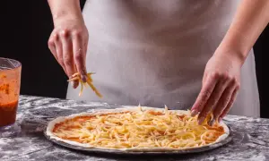 Ręce posypują pizzę startym serem. Zastanawiasz się, jaki ser do pizzy będzie najlepszy? Ten wygląda apetycznie!