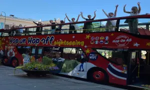 Glada resenärer vinkar från övervåningen på en röd dubbeldäckare med texten "Hop on Hop off sightseeing".