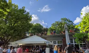 Menschen genießen das Wetter im Golgatha Biergarten. Sonnenschein, grüne Bäume und ein blauer Himmel bilden die Kulisse.