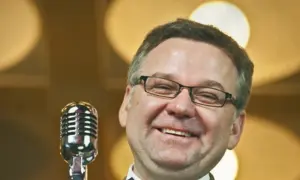 Artur nagrał płytę myśliwiecka. Uśmiechnięty mężczyzna w okularach stoi przy mikrofonie.