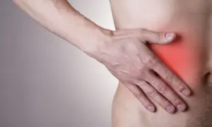 Dłoń uciska prawy bok, gdzie widoczny jest czerwony obszar bólu pod żebrem.