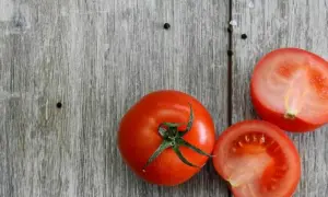 Tomates frescos, uno entero y dos cortados por la mitad, sobre una tabla de madera. Son un ejemplo de 10 alimentos umami.