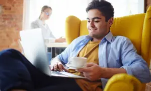 Młody mężczyzna z kawą na laptopie, szukający sposobów, jak stać się bardziej widocznym w internecie.