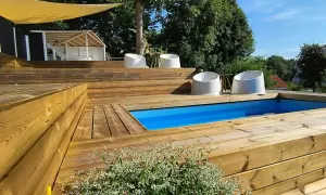 En härlig altan med nivåskillnad och pool. Vita stolar står utplacerade på de breda trätrappstegen.