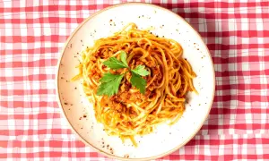 Assiette de spaghetti à la bolognaise, garnie de persil frais, sur une nappe à carreaux rouges et blancs. Une question se pose : peut-on manger des pâtes le soir ?