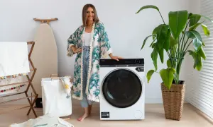 Kobieta w kwiecistej narzutce obok nowoczesnej pralki Haier. Wiele osób szuka pralki Haier opinie, by wybrać najlepszy model.