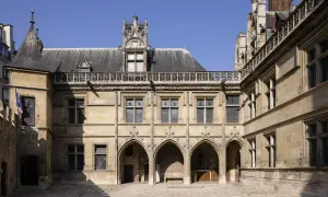 Hof des Musée de Cluny mit gotischer Architektur, Spitzbögen und filigranen Verzierungen unter blauem Himmel.