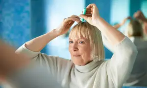 Kobieta stosuje preparat na skórę głowy, by zaradzić problemowi, jakim jest menopauza a wypadanie włosów.