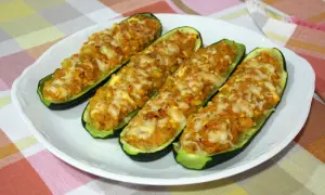 Cuatro calabacines rellenos, gratinados con queso, servidos en un plato blanco sobre un mantel a cuadros.