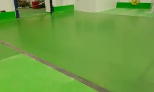 Suelo de nave industrial de color verde brillante, con un desagüe metálico en diagonal.