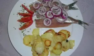 Matjes mit Bratkartoffeln, garniert mit Zwiebelringen und Tomaten. Ein klassisches Gericht, das auf einem weißen Teller serviert wird.
