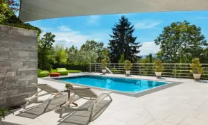 Moderne poolumrandungen ideen: ein rechteckiger Pool mit türkisfarbenem Wasser, umgeben von hellen Terrassenplatten, Liegestühlen und grünen Sitzsäcken.