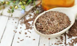Łyżka pełna siemienia lnianego, naturalnego sposobu na zaparcia. W tle widać łuskę lnu i butelkę oleju.