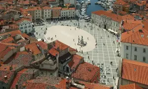 Widok na plac w Piran, Słowenia, z widokiem na morze i port. Czerwone dachy i zabytkowa architektura tworzą malowniczy krajobraz.