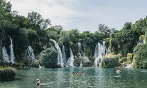 Atemberaubende Wasserfälle in Bosnien, Natur pur. Menschen genießen das kühle Wasser in einem türkisfarbenen See, umgeben von üppiger Vegetation.
