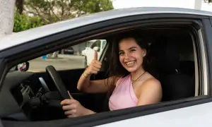 Joven sonriente en coche, pulgar arriba. ¡Ya sabe hasta que edad se puede conducir en España!