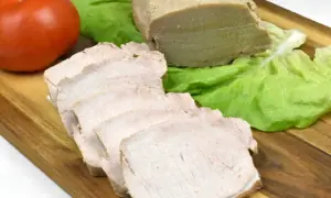 Pokrojony schab gotowany w majonezie, liście sałaty i pomidor na desce.