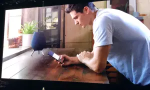 Un homme utilise son téléphone pour contrôler son **galaxy home**. Un haut-parleur intelligent est visible sur la table.