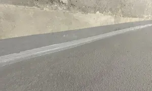 Szara posadzka z widoczną dylatacją wypełnioną białym materiałem, granicząca z betonową ścianą.