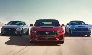 Tre Ford Mustang modeller i rött, grått och blått kör på en ökenväg.
