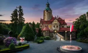 Zamek Czocha o zmierzchu, z fontannami i kwitnącymi krzewami. Bilety do zamku warto kupić wcześniej, by uniknąć kolejek.
