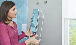 Dziewczyna z lustrem w rękach, przygotowuje się do montażu. Pokazuje, jak przykręcić lustro do ściany.