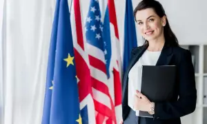 Donna sorridente con cartella, sullo sfondo bandiere UE, USA e Francia. Un futuro in scienze investigative triennale.