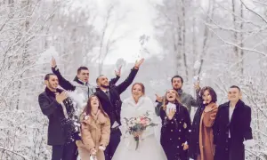 Brautpaar und Gäste werfen Schnee in der Luft. Perfekt für eine Hochzeit im Winter: Was anziehen? Warme Mäntel und festliche Kleidung.