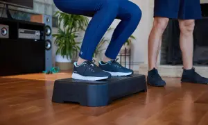 Person macht Kniebeugen auf einer Aerobic-Plattform. Die **step aerobic schuhe** sind dunkelblau mit hellblauen Akzenten.