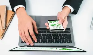 Dłonie na laptopie i smartfonie z wykresami, obok notatniki.