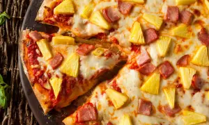 Pyszna hawaiian pizza z kawałkami ananasa i szynki, obficie posypana serem, prezentuje się apetycznie na ciemnym tle.
