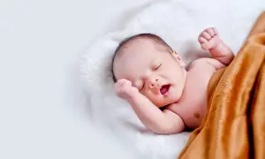 Śpiący noworodek otulony kocykiem. Pamiętaj o odpowiedniej, jaka temperatura mleka dla noworodka, by zapewnić mu komfort.