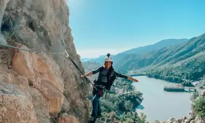 Aventura en el Caminito del Rey. Mujer sonríe mientras recorre la vía ferrata, con un embalse y montañas de fondo.