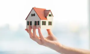 Dłoń trzyma model domu z czerwonym dachem. Marzenie o własnym domu, które wymaga pozwolenie na budowę.