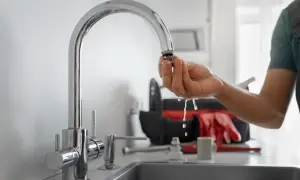 Instrukcja, jak usunąć kamień z kranu: hydraulik pokazuje wyczyszczony aerator, z którego kapie woda. W tle torba z narzędziami.