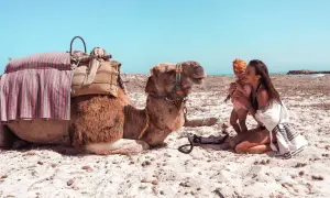 Djerba plaże: matka z dzieckiem i wielbłąd na piasku pod błękitnym niebem.