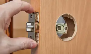 Dłoń wsuwa metalowy mechanizm zamka do otworu w drewnianych drzwiach.