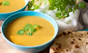 Zupa krem z soczewicy w niebieskich miseczkach, udekorowana kolendrą, obok chlebki naan.