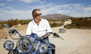 Mężczyzna w okularach przeciwsłonecznych na motocyklu w pustynnym krajobrazie. Czy to jego sposób na odpowiedź, ile trwa kryzys wieku średniego?