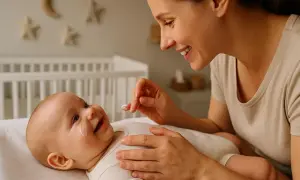 Uśmiechnięta mama delikatnie aplikuje krem na policzek niemowlaka, dbając o higienę jamy ustnej noworodka.